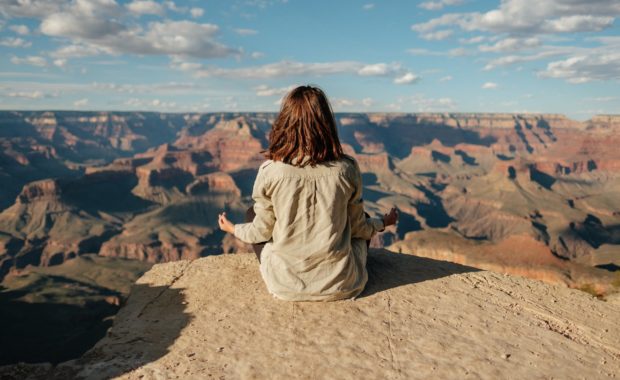 woman in white jacket sitting on brown rock
